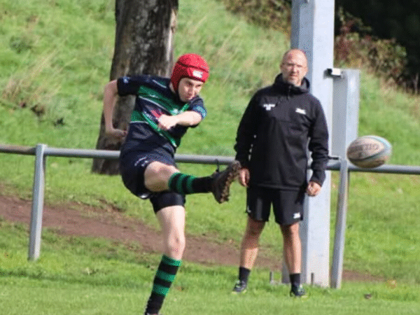 Young man kicking rugby ball at rugby match.